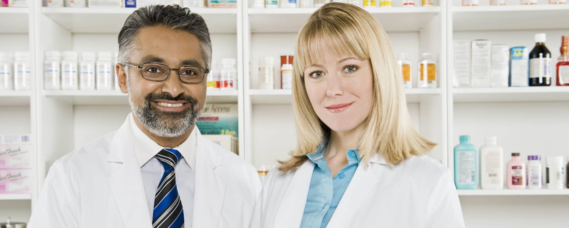 Portrait of a happy middle aged pharmacist standing with mature colleague at workplace